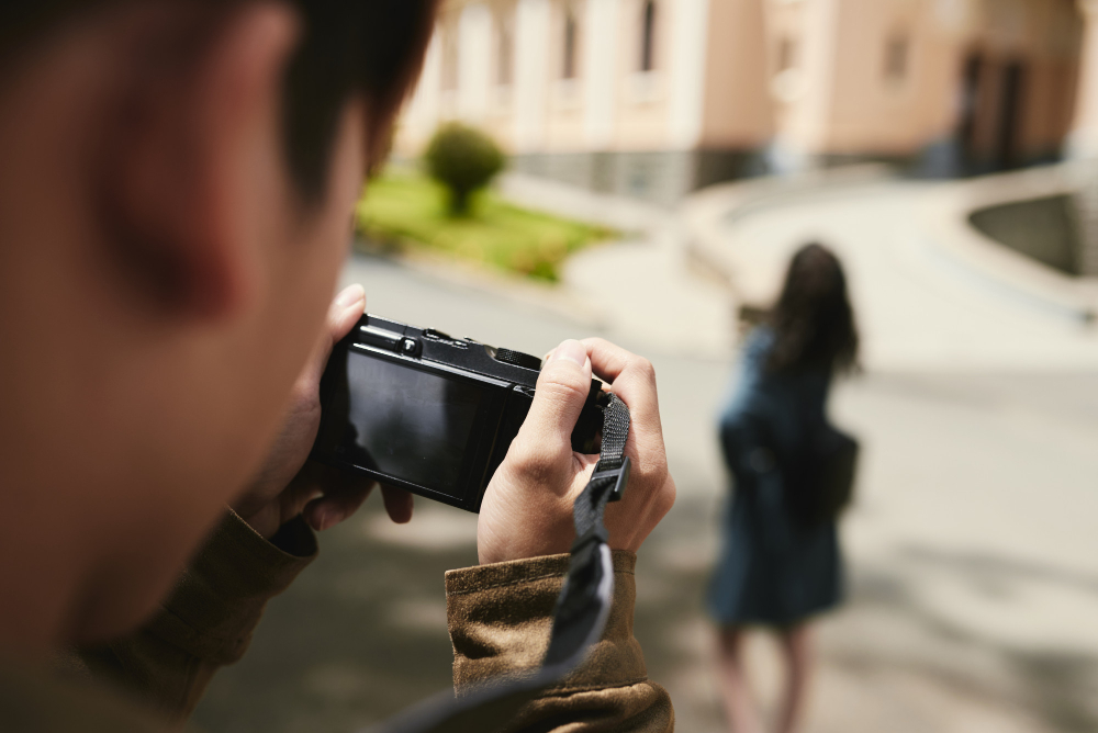 A private investigator takes a photo of a woman walking ahead, using a digital camera, to gather adultery evidence, with a focus on the camera's display screen.