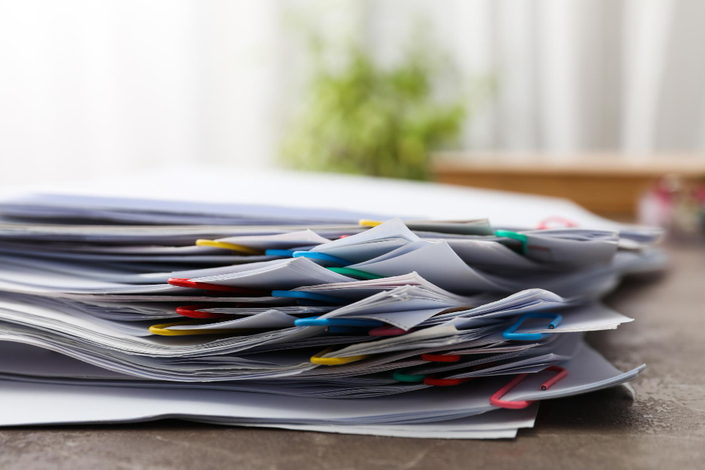 A stack of organized documents related to hiring a private investigator, with colorful paper clips on a wooden desk, blurred background.